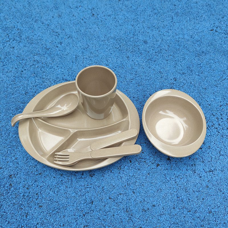 Rice husk kids tableware set — divided plate, cup, bowl, fork and spoon on a blue textured background