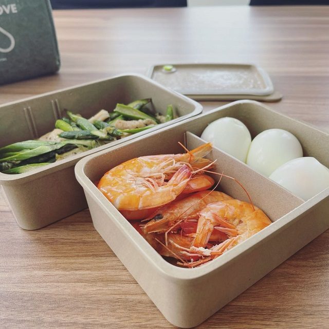 Rice husk lunch box served in a cafe or takeaway setting — showing shrimp, vegetables and eggs, illustrating restaurant / catering use