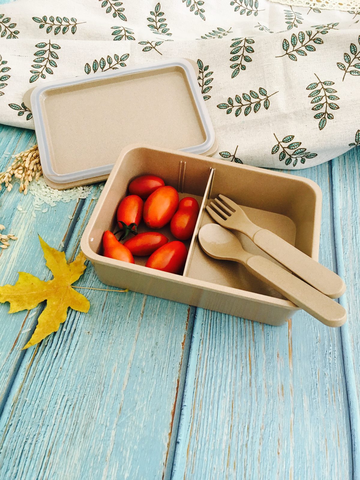 Rice husk lunch box paired with reusable fork and spoon on a rustic wooden table, with tomato garnish