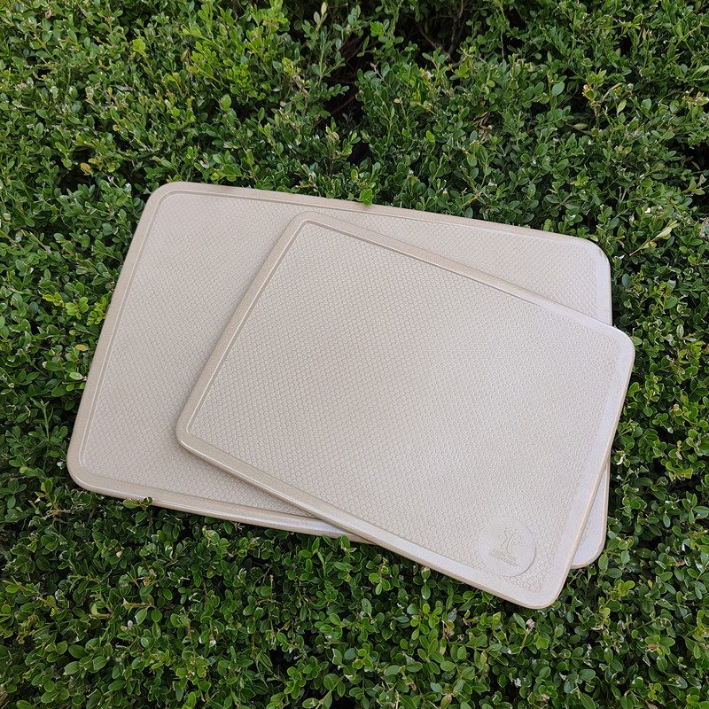 Two rice husk chopping boards in natural beige, photographed outdoors on green shrubs
