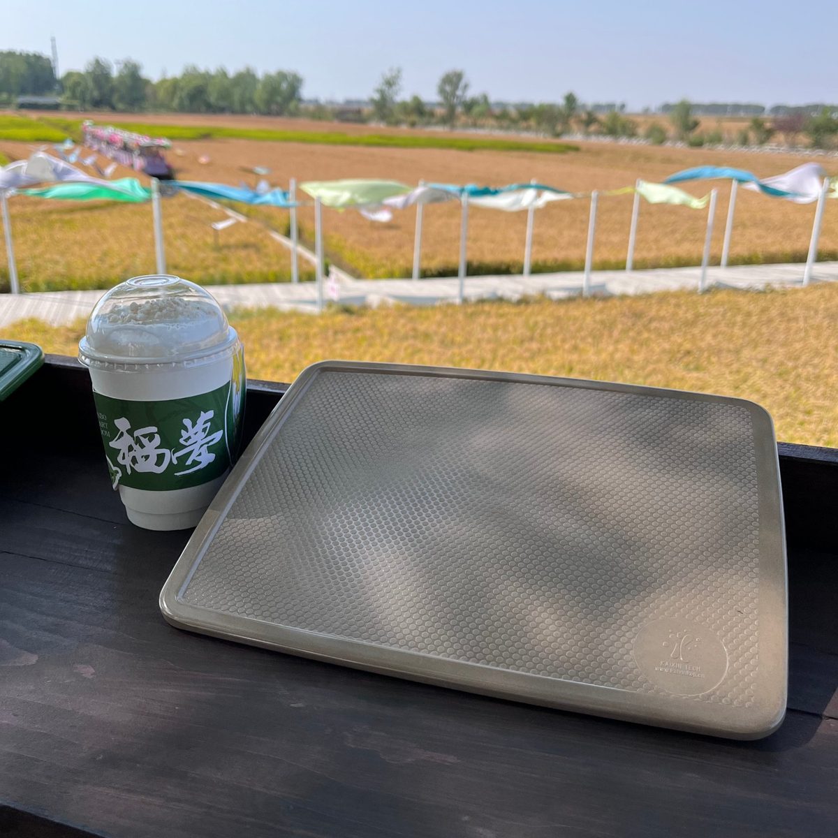 Rice husk serving tray photographed on a viewing deck beside a rice field — lightweight, giftable eco tableware for holiday retail