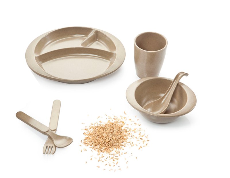 Rice husk kids dinnerware set beside a pile of raw rice husks — the agricultural byproduct the tableware is molded from